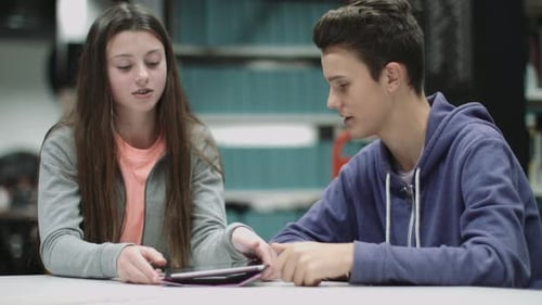 Teenage boy and girl working on digital tablet in library