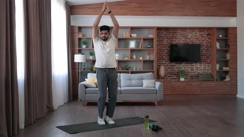 Bärtiger arabischer Mann in Sportkleidung springt auf Yogamatte