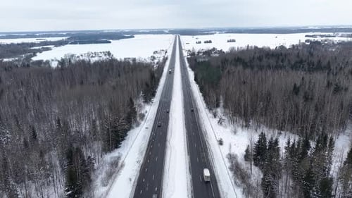 Aerial View of Snowy Road Through Winter Forest Landscape