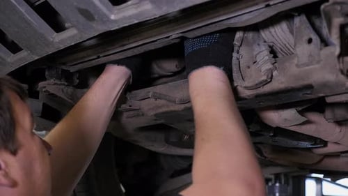 Closeup of a Mechanic with a Screwdriver Repairing a Car at a Service Station