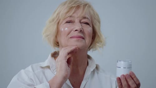 Senior woman applying face cream in bright setting