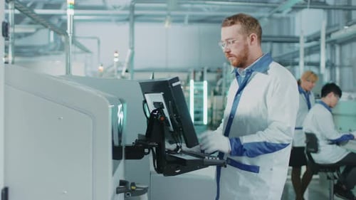 On High-Tech Factory Male Engineer Uses Computer for Programing Pick and Place Electronic Machinery