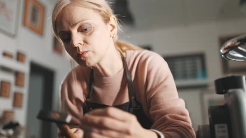 Focused Female Jeweler Hammering Metal in Workshop