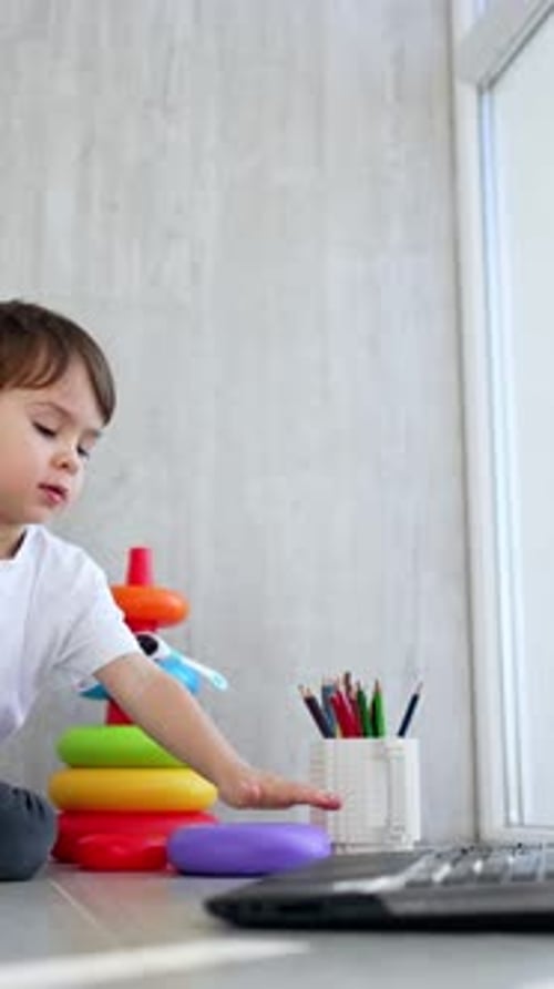 Un hermoso niño pequeño con una camiseta blanca se sienta en el suelo cerca de la pirámide de juguetes.
