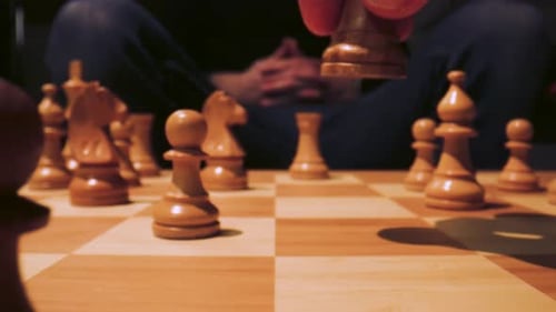 Folgende Aufnahme einer Hand, die eine Schachfigur auf einem riesigen Schachbrett spielt.