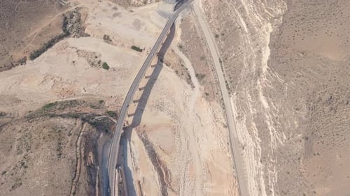 Aerial View of a Concrete Bridge and Winding Mountain Roads with Moving Vehicles in an Arid Desert