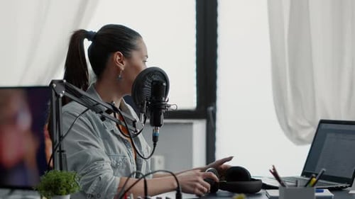 Creative Podcast Host Sitting in Studio at Desk While Talking to Audience