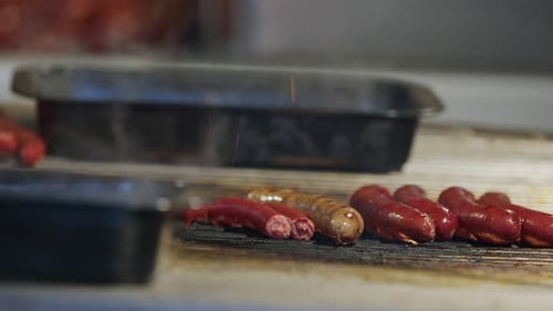 Sausages Cooking on a Grill with Silver Tongs