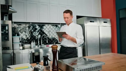 Professional chef using tablet computer for recipes while working in modern kitchen cooking concept