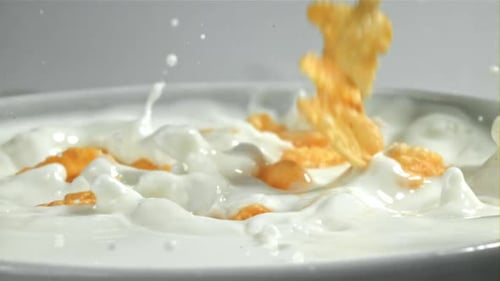 Crispy Corn Flakes Splashing into Milk in Bowl
