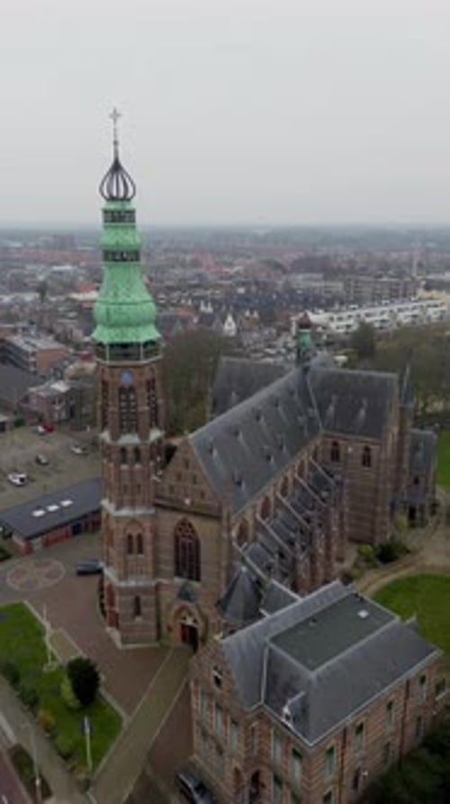 Aerial view of a tall church tower with a green spire, surrounded by a quiet town, roads