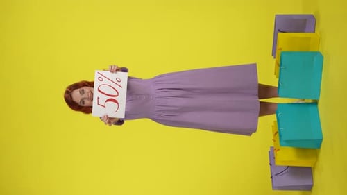 Happy Redhaired Woman Surrounded By Shopping Bags Holding a Poster with the Inscription Fifty