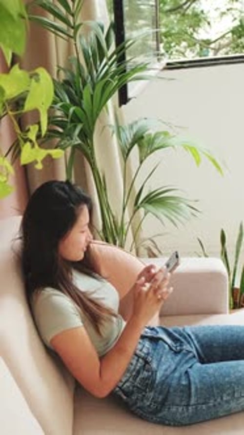 Young woman sitting on a sofa with a mobile phone in her hands, view from above