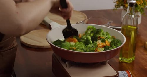 Cooking broccoli and carrots in frying pan indoors