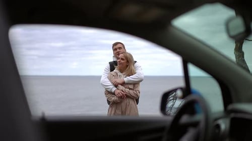 Loving Couple Embraces on Beach Viewed Through Car