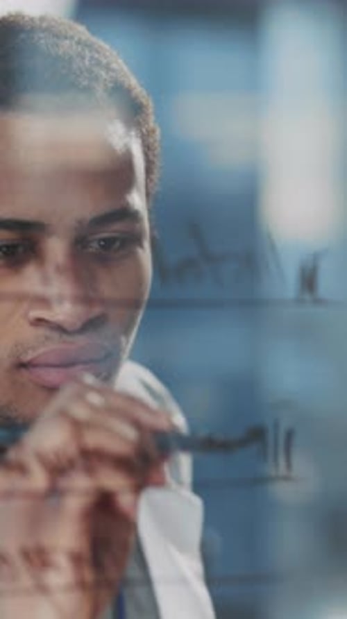 Young Male Clinician Uses Markers to Illustrate Research Notes on Reflective Glass Surface in