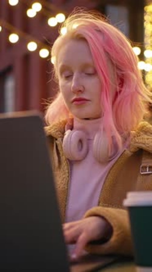 Young Pink Haired Stylish Woman Working on Laptop Sitting Outdoors with Takeout Coffee and Computer