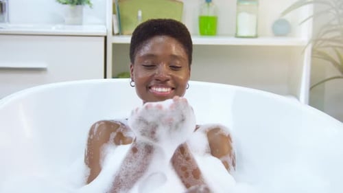 Woman Relaxes in Bubble Bath and Blows Bubbles
