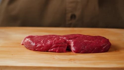 Hands place raw beef steaks on cutting board