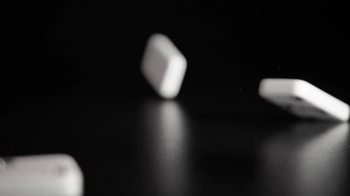 White domino dice fall on a black background. Slow motion