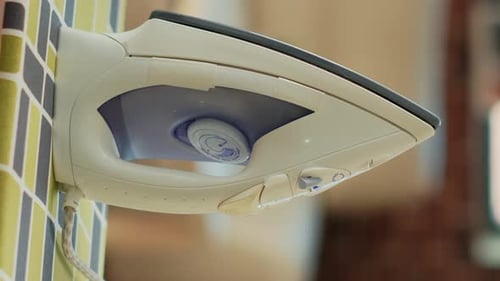Vertical Video Iron Tool Placed on Ironing Board with Pile of Washed Clothing