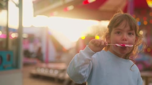 Girl Enjoys a Lollipop at a Carnival at Sunset