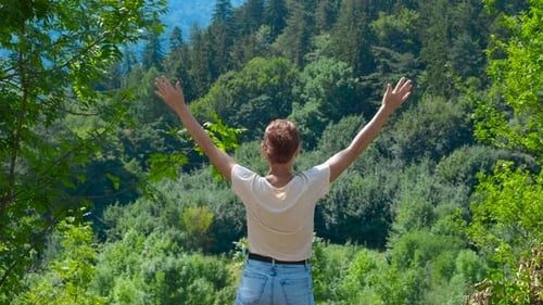 Frau hebt die Arme und genießt den Blick auf den grünen Wald