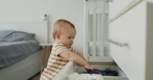 Baby Plays With Clothing Inside an Open Drawer