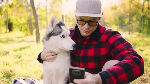 Sitting on a Cozy Blanket in an Autumn Park a Young Man in a Plaid Shirt and Cap Snaps a Fun Selfie