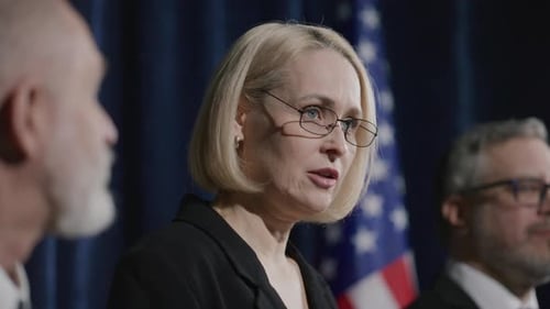 Woman Speaking at Press Conference with American Flag