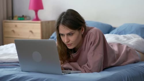 Woman Using Laptop While Lying on Bed