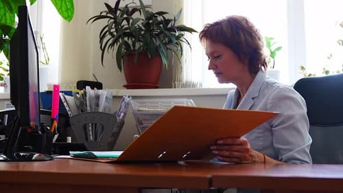 Woman Working with Folders and Documents at Her Desk in an Office Setting Paperwork Routine Archive