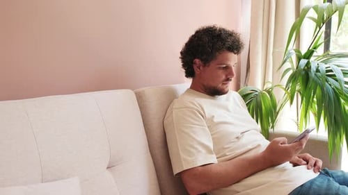 Young Adult Using Smartphone on Sofa Indoors
