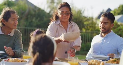 Happy diverse family eating lunch together outside in the garden at home