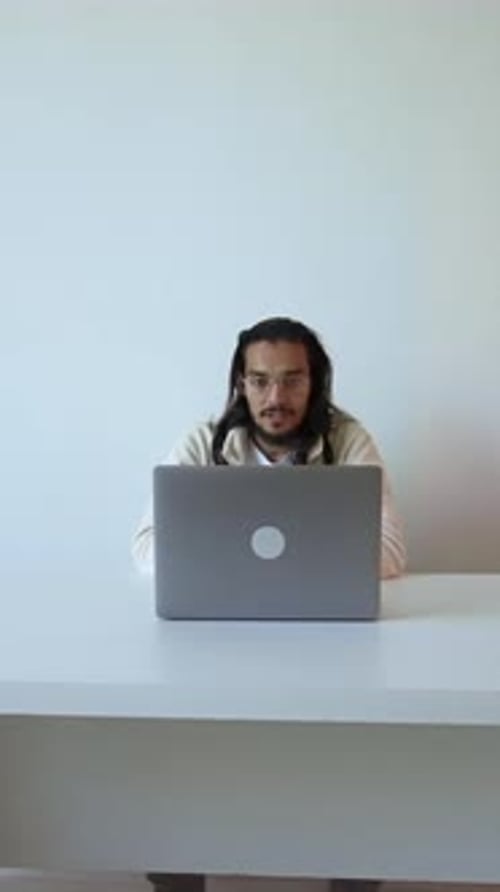 Man at Desk with Laptop Puts Glasses Away