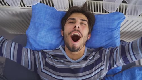 Young Man Waking Up and Stretching in Bed