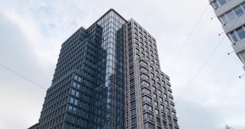 Skyscraper against cloudy sky, low angle view. Camera panning left