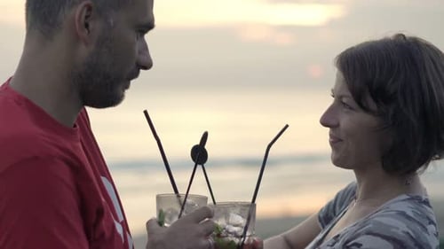 Young couple raising cocktails in a terrace cafe enjoying a romantic sunset view
