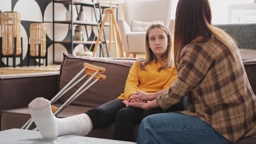Mother Comforting Teen Daughter with Broken Leg at Home