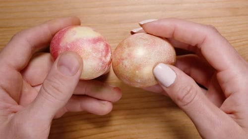 Hands holding two marbled pink-yellow Easter eggs, preparing to tap them together, symbolizing an