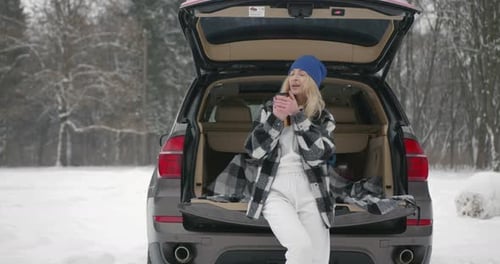 Young Woman with Hot Drink Near Car at Winter Forest
