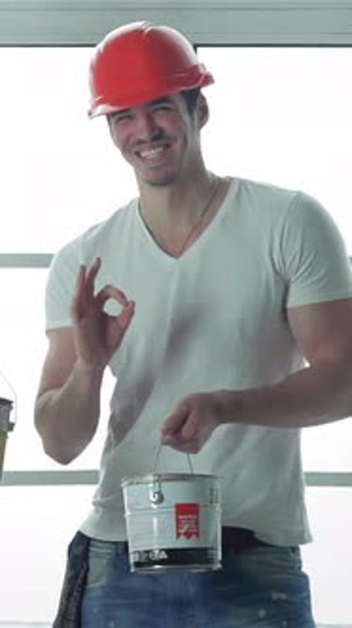 Smiling construction worker holding paint can gives OK sign
