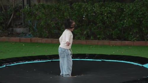 Little Girl Jumping on Trampoline Outdoors in Backyard