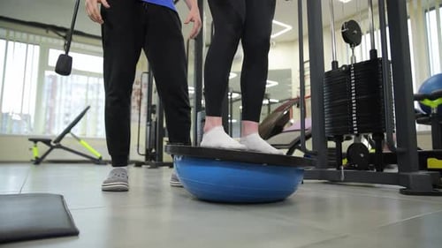 Man Doing Balance Exercises on Bosu Ball Under the Guidance of a Specialist in a Fitness Studio