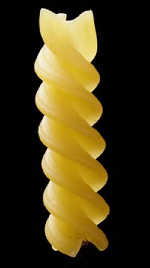 A lonely fusilli pasta, spinning in a spiral on a black background, close-up. Vertical video.