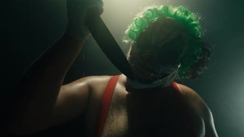 Scary Man in the Horror Clown Mask with Green Hair Standing in Suspenders in the Dark Studio with