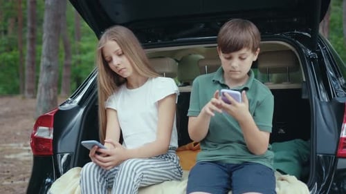 Siblings Using Cell Phones in Car Trunk