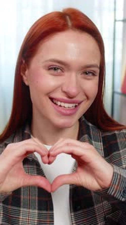 Smiling Woman Makes Heart Shape with Hands Indoors