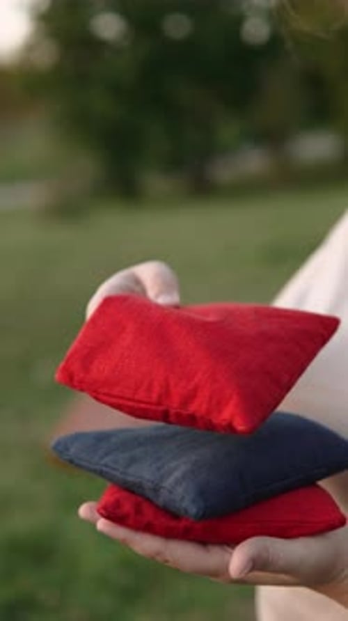 Vídeo vertical de una persona apilando coloridas bolsas de cornhole sobre la mano de un jugador