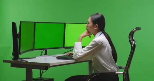 Asian Woman Thinking While Working With Mock Up Multiple Computer Monitor In Green Screen Studio